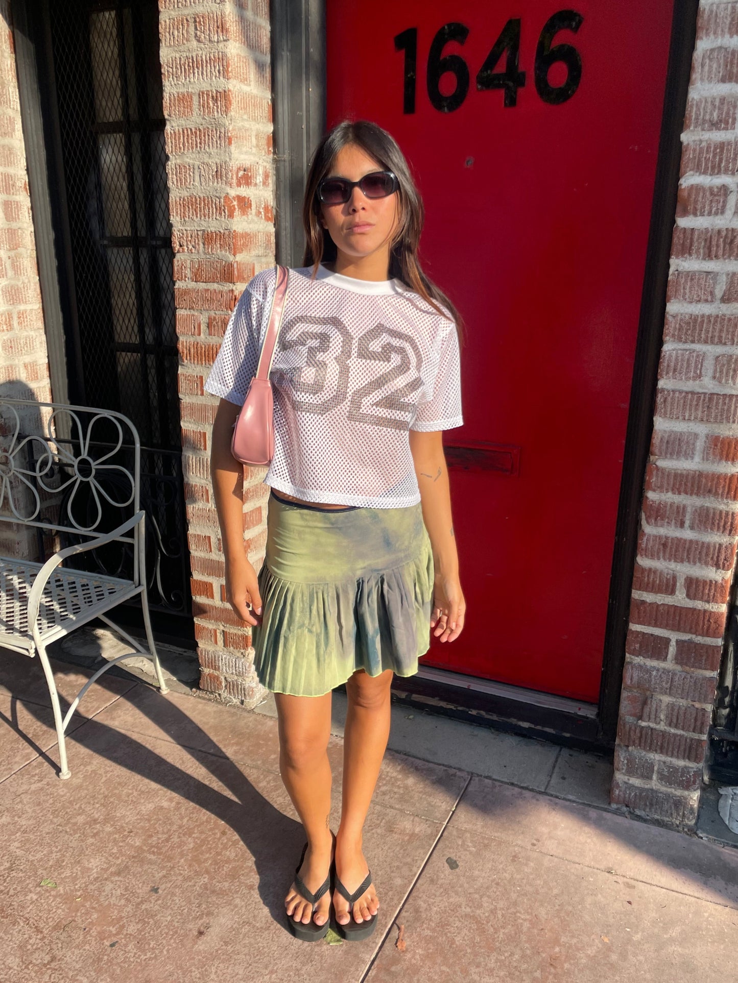 Person lying on a red door with number 1646, wearing a white top with numbers and green skirt.