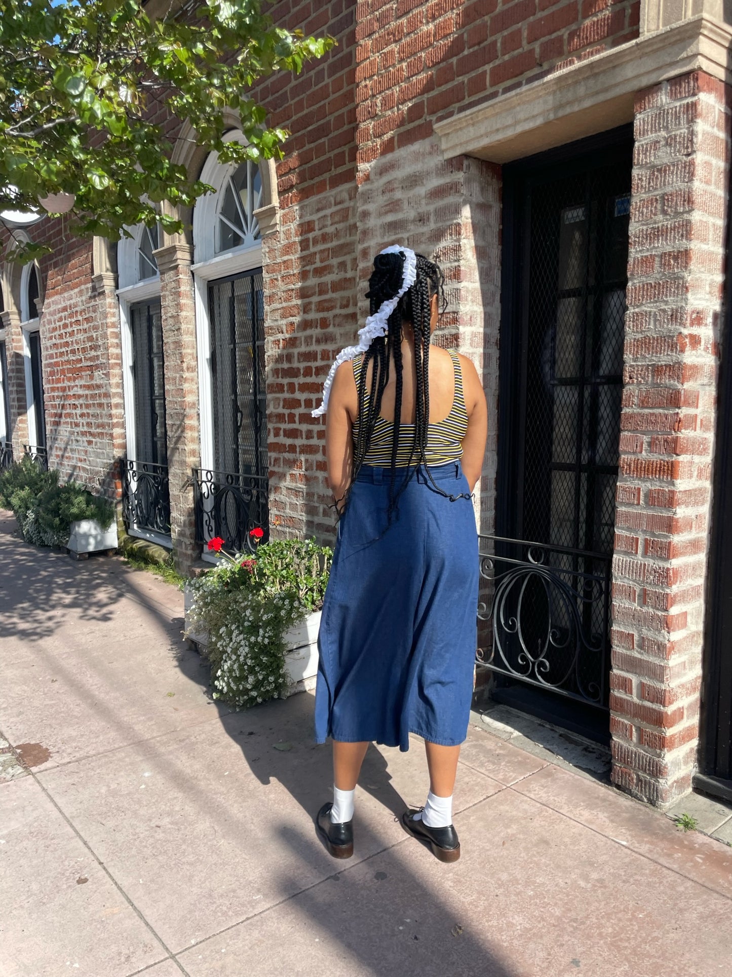 back of girl wearing long blue jean skirt and crochet purse and white yellow and black striped shirt