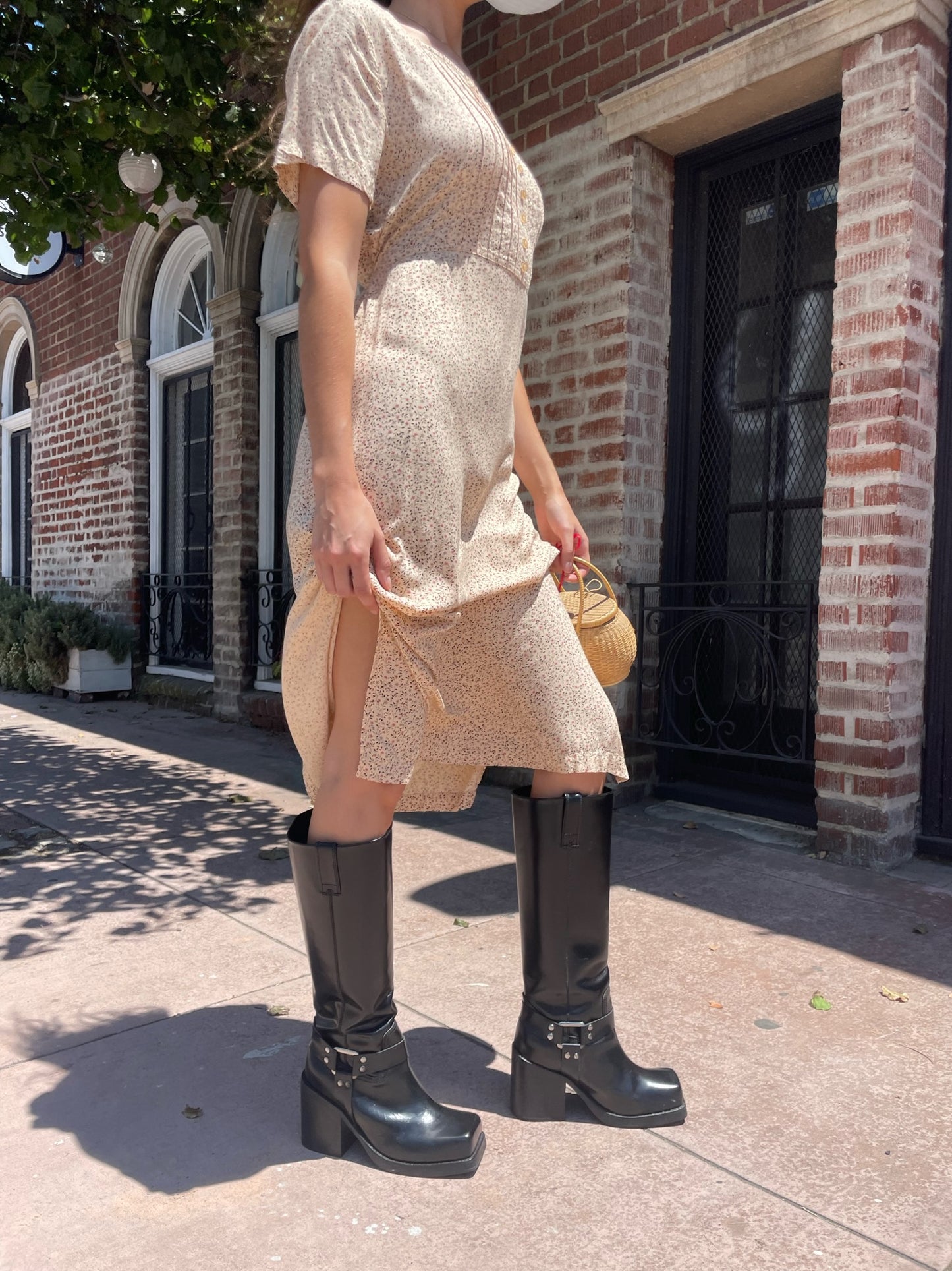 girl wearing cream floral dress, wicker handbag, and black leather boots