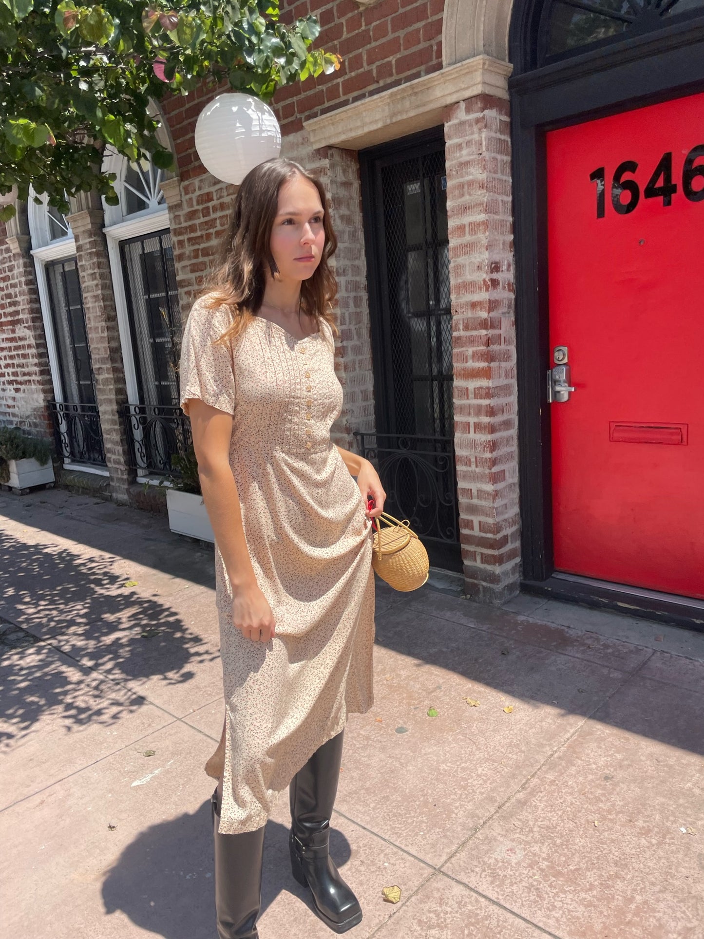 girl wearing cream floral dress, wicker handbag, and black leather boots