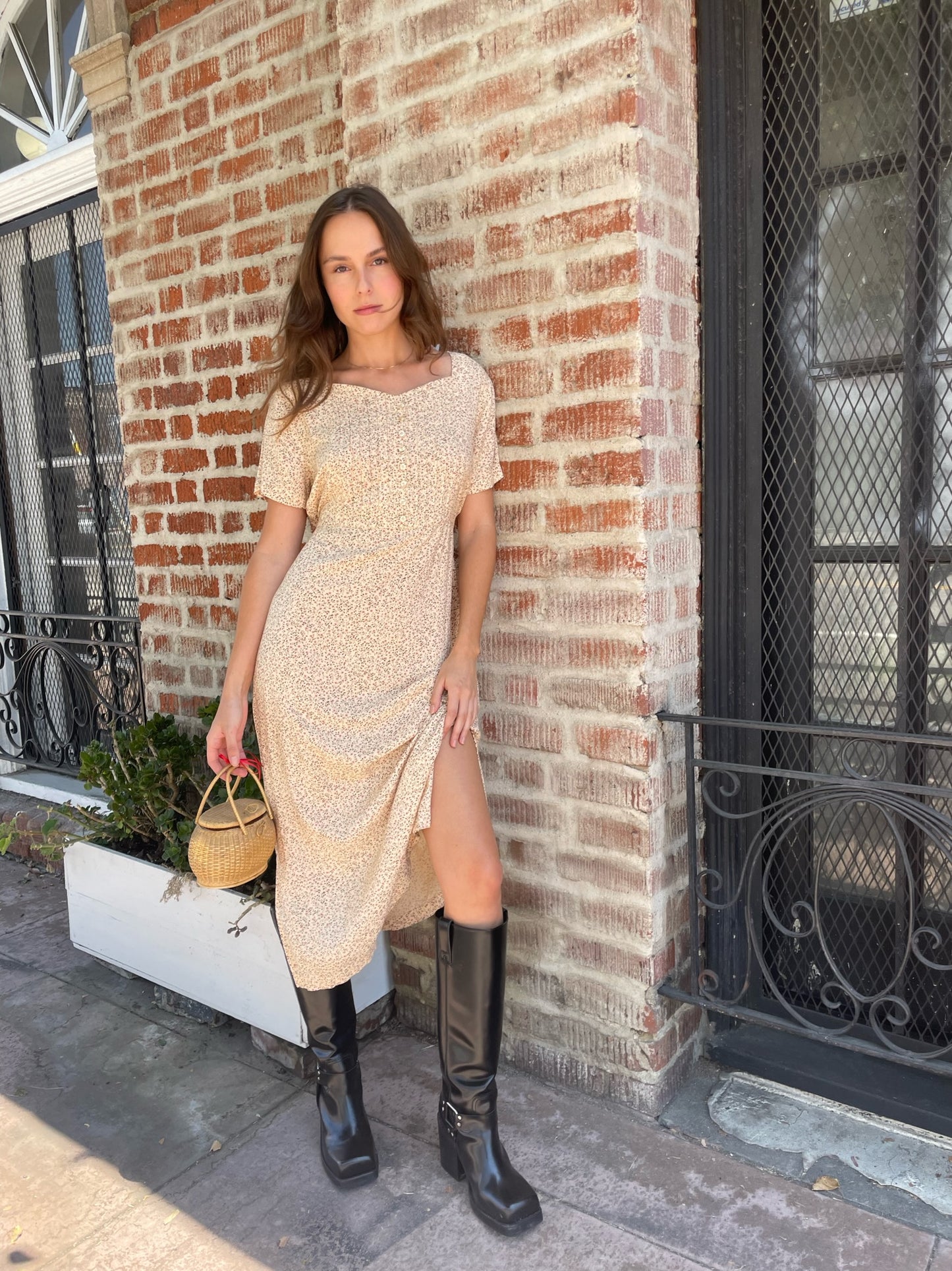 girl wearing cream floral dress, wicker handbag, and black leather boots