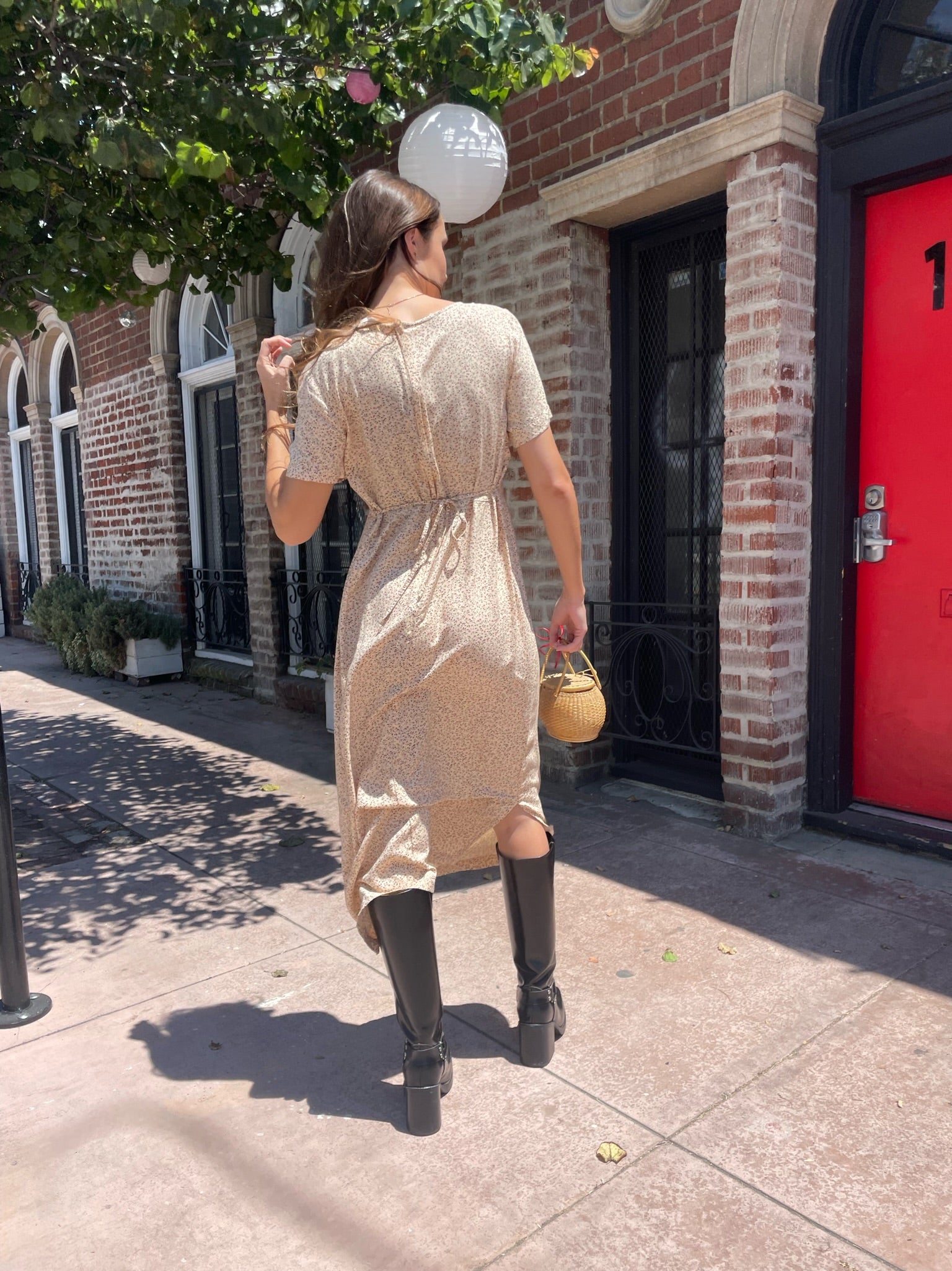 back of girl wearing cream floral dress, wicker handbag, and black leather boots