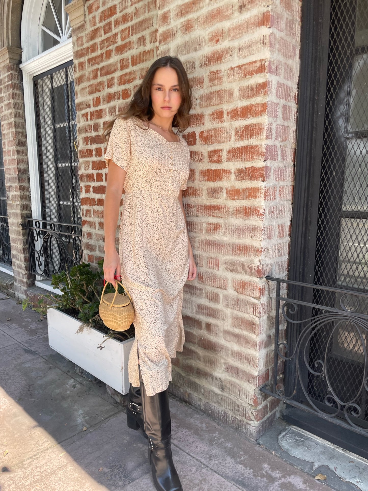 girl wearing cream floral dress, wicker handbag, and black leather boots
