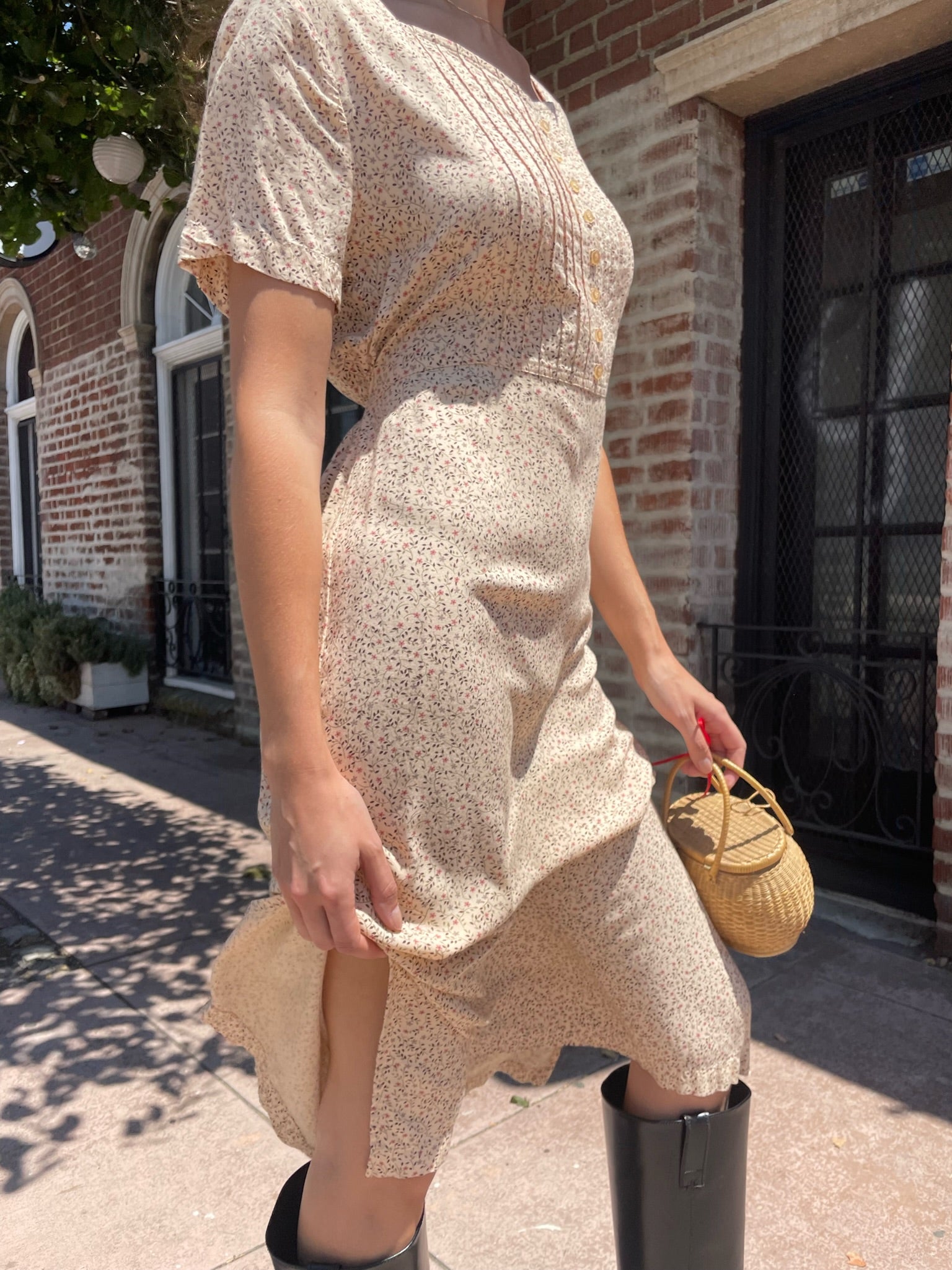 girl wearing cream floral dress, wicker handbag, and black leather boots