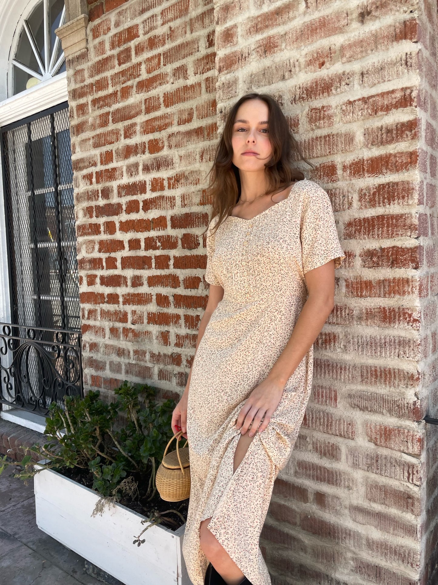 girl wearing cream floral dress, wicker handbag, and black leather boots