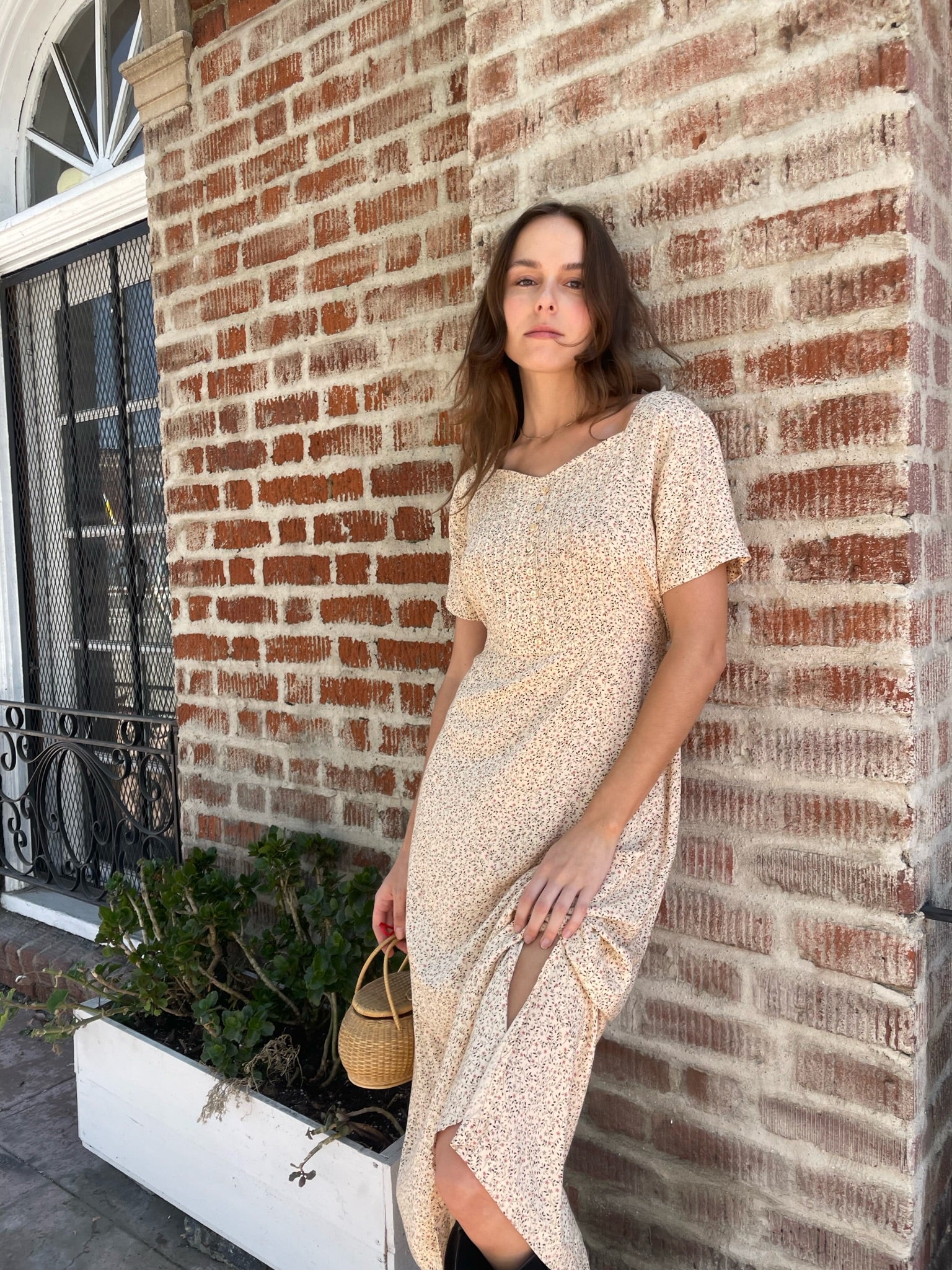 girl wearing cream floral dress, wicker handbag, and black leather boots