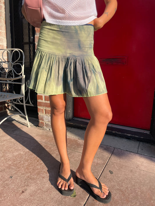 Person wearing a green skirt and black sandals on a sidewalk.