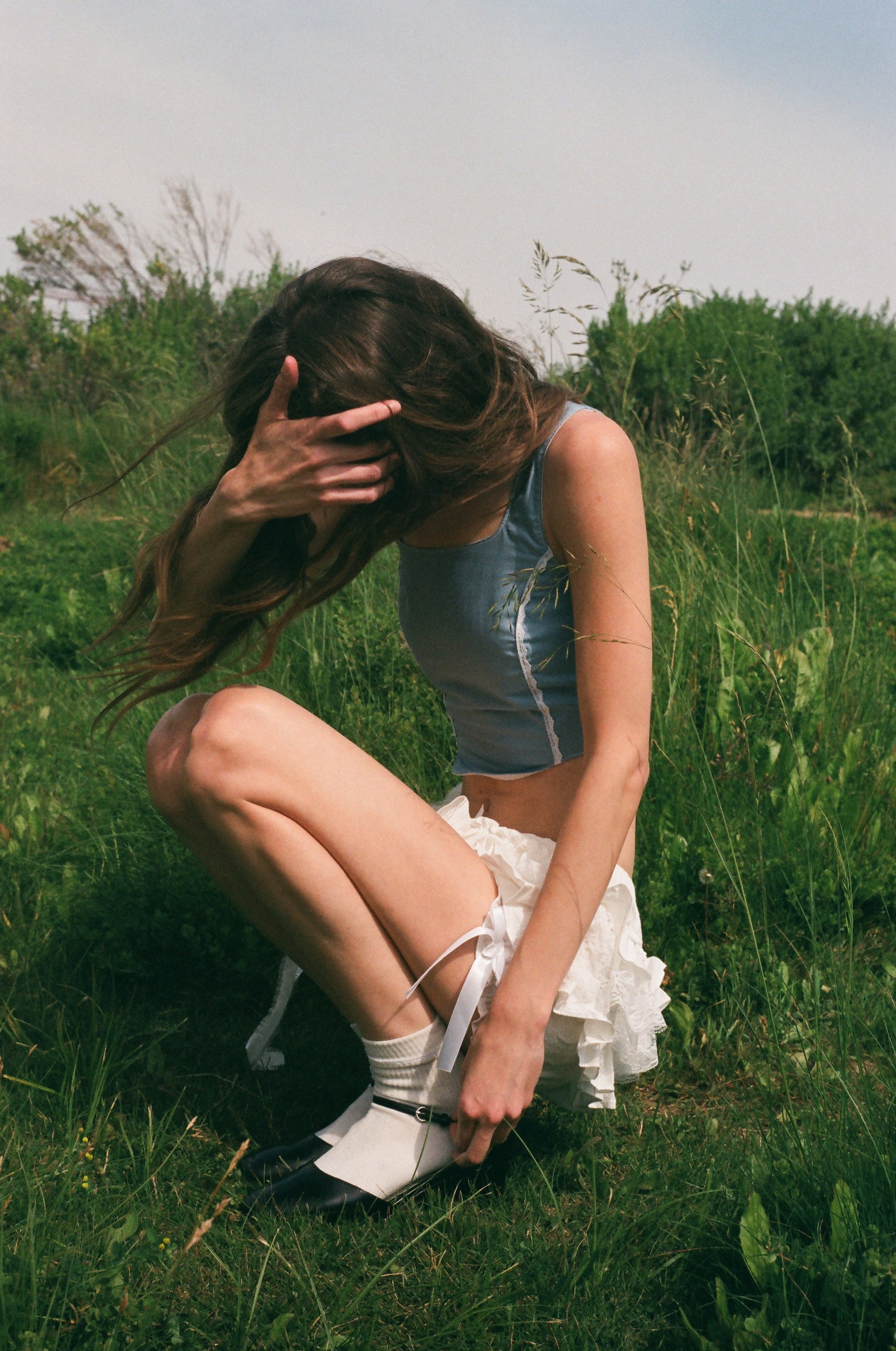 girl crouching in a green field wearing a blue corset and white ruffle bloomers