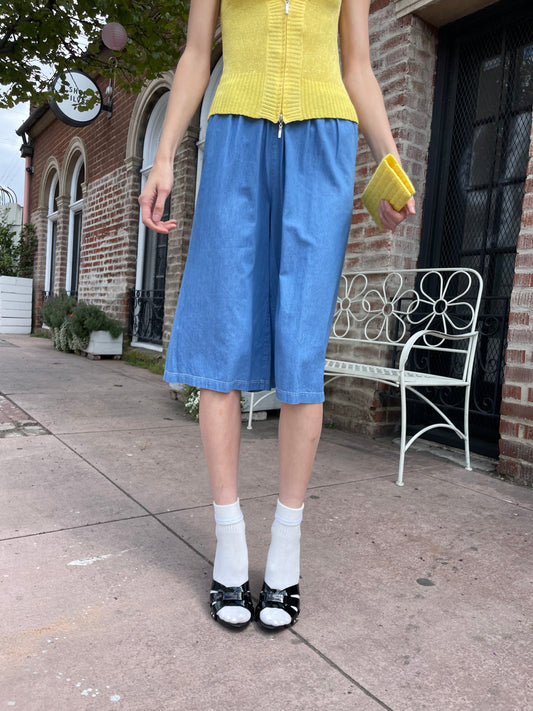 girl wearing yellow crochet top and long blue shorts with yellow clutch