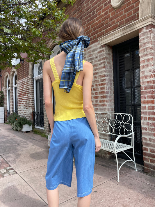 girl wearing yellow crochet top and long blue shorts with yellow clutch