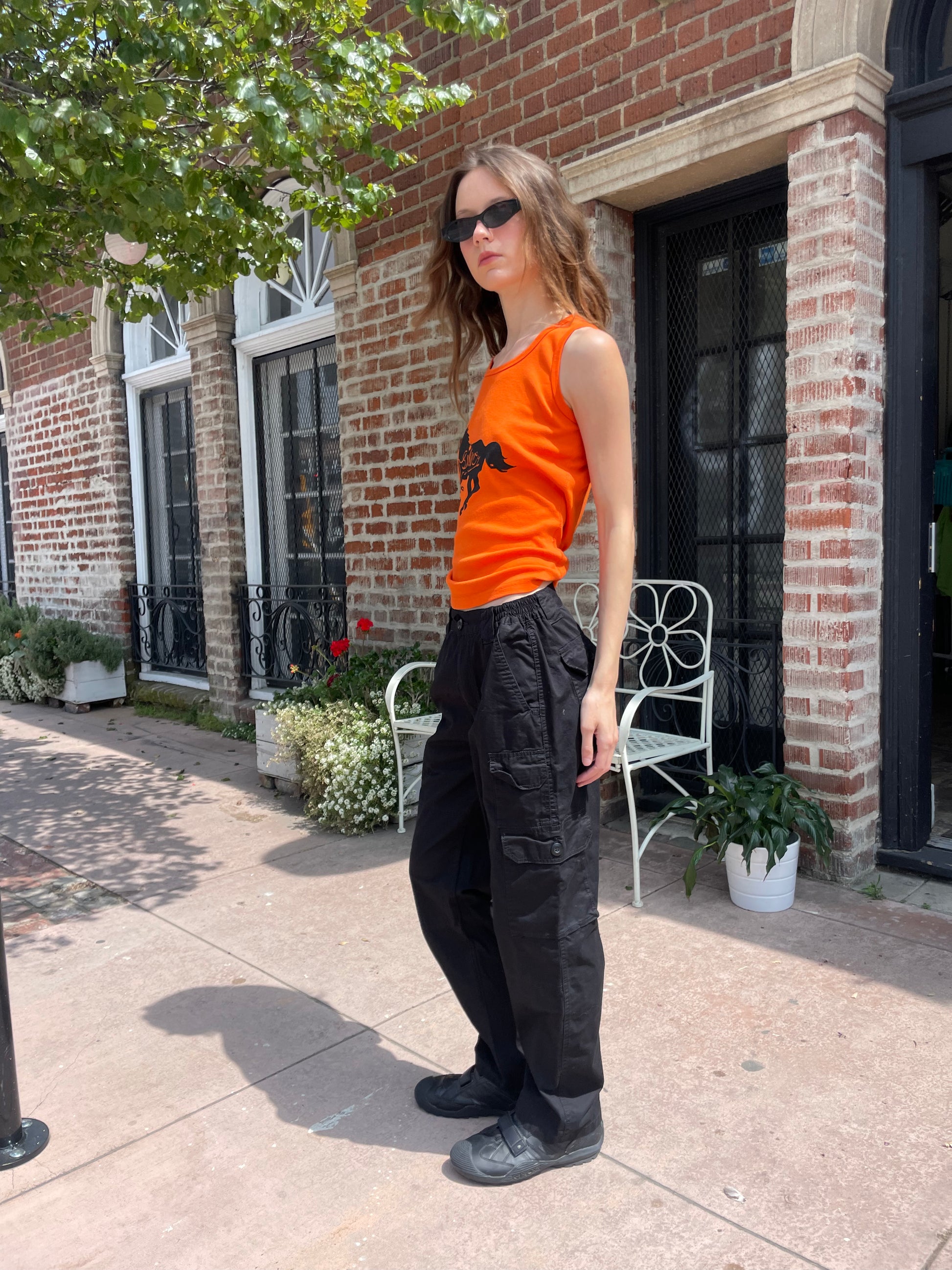 profile of girl wearing orange tank top black cargo pants and black sunglasses