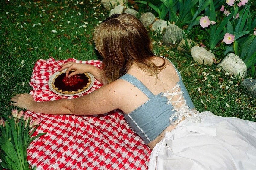 girl eating cherry pie wearing a blue corset and white skirt