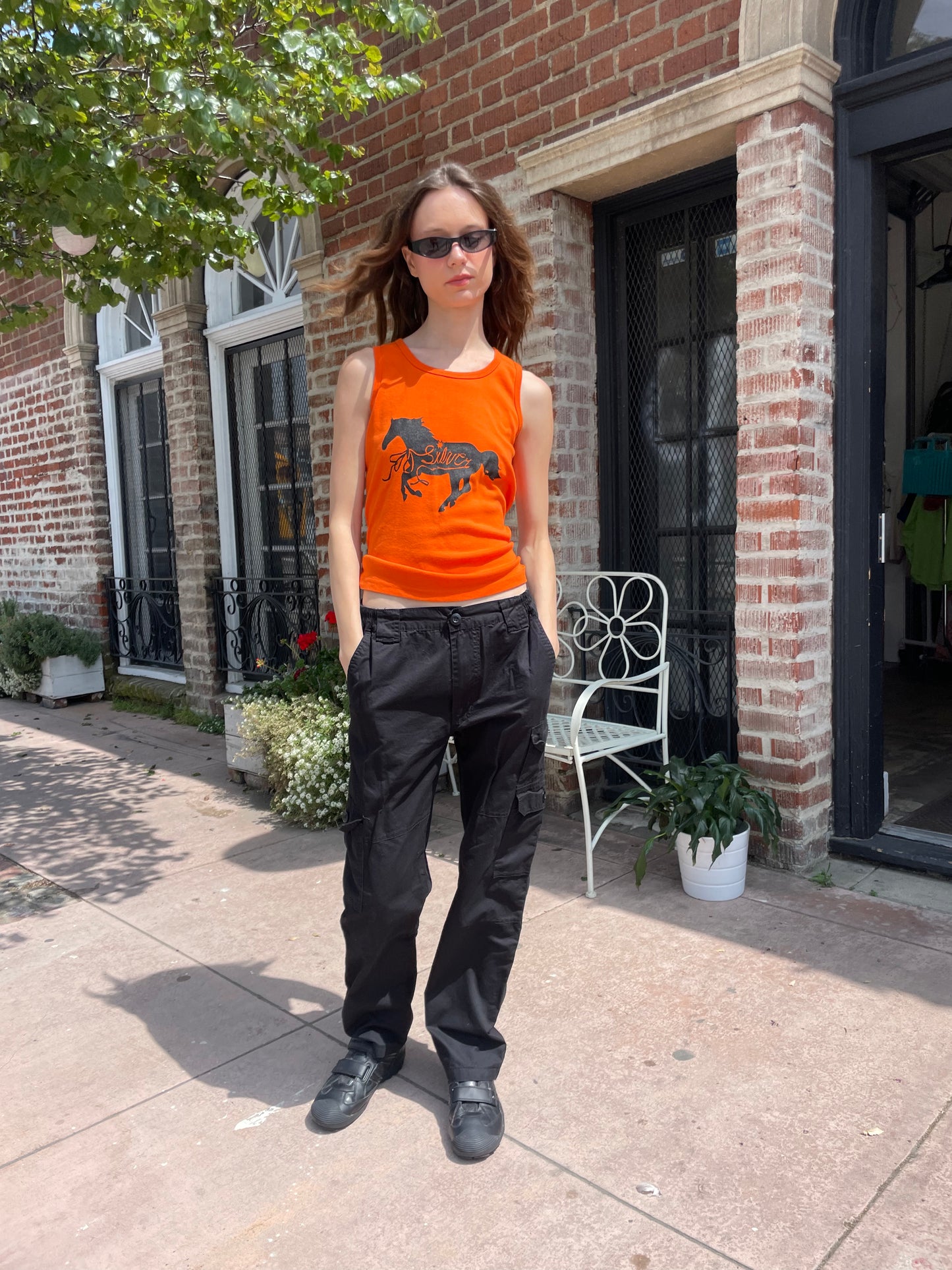 girl wearing orange tank top black cargo pants and black sunglasses