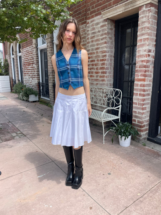  girl wearing blue plaid vest, white skirt and black boots