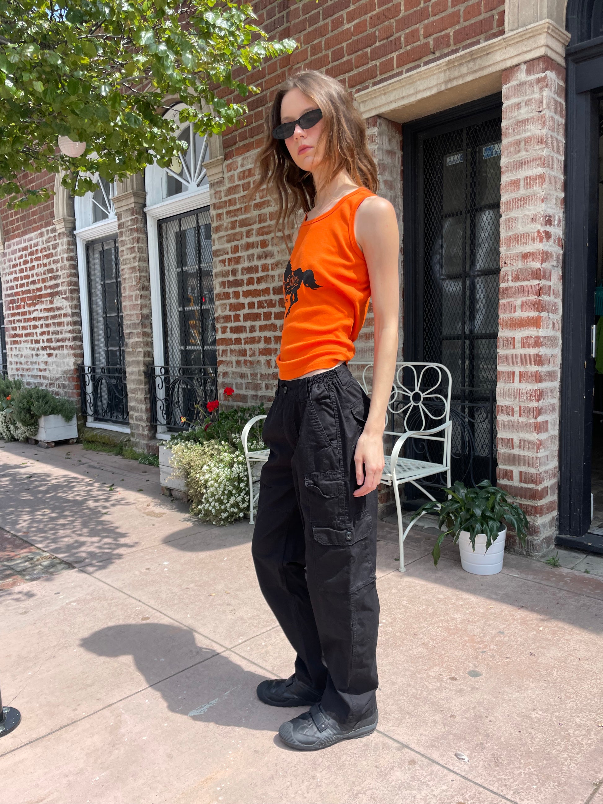 girl wearing orange tank top black cargo pants and black sunglasses