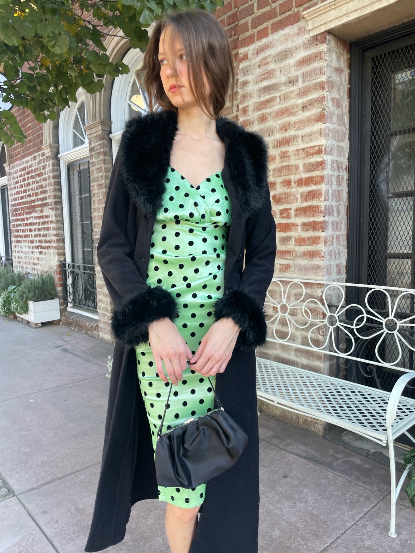 girl wearing a black fur collar coat with green polka dot dress