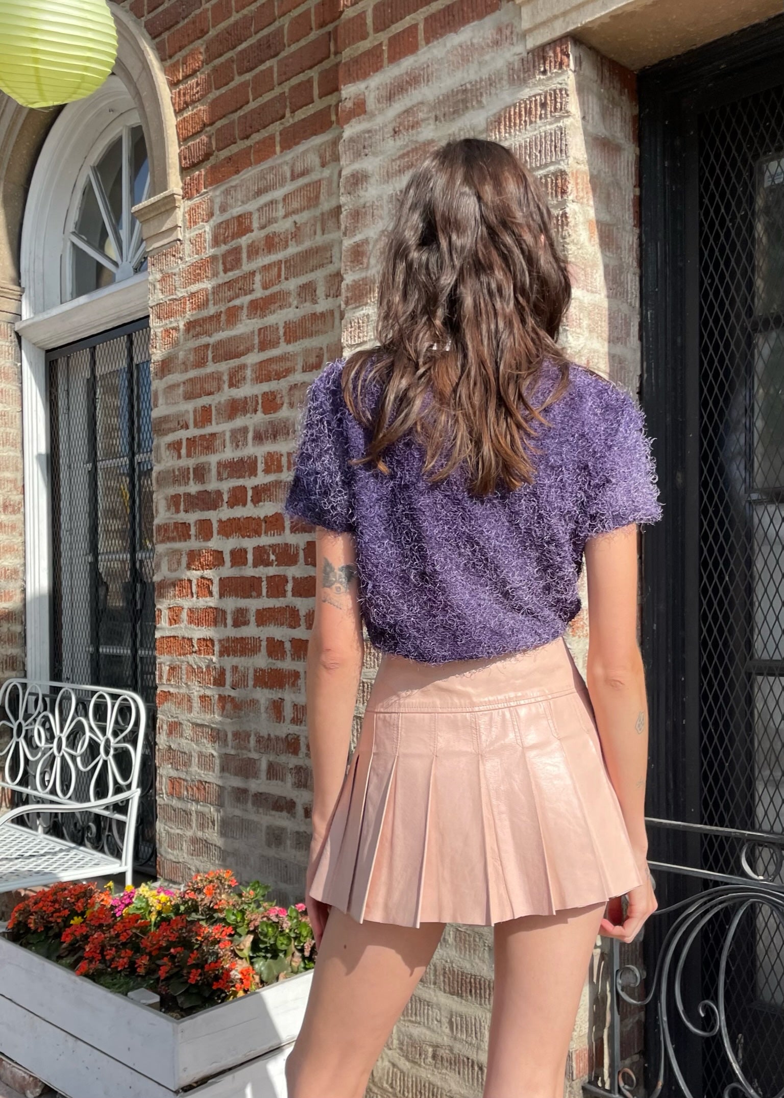 back of girl wearing textured purple shirt and leather pink pleated skirt