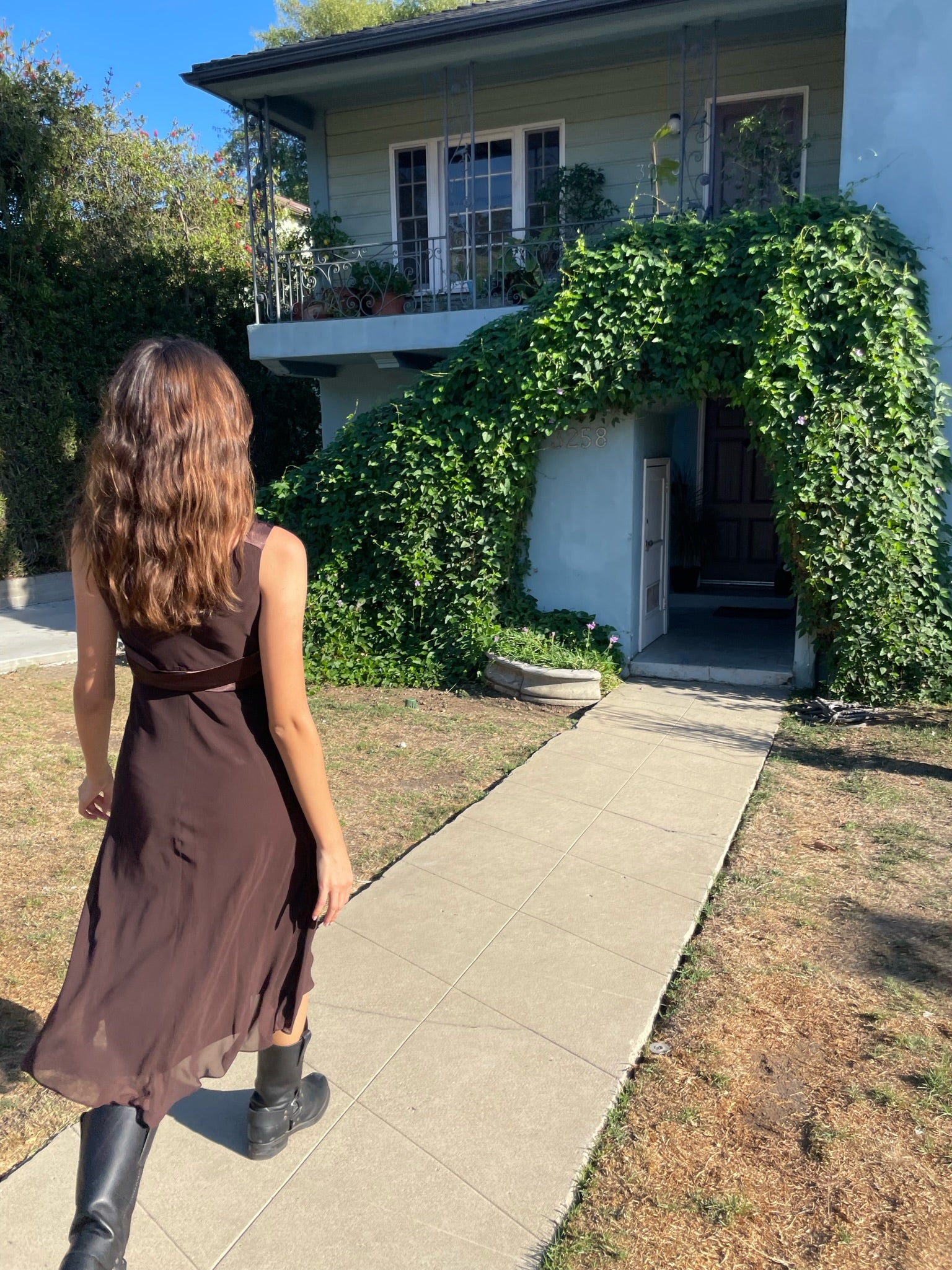 back of girl walking down a sidewalk wearing a brown dress and black boots