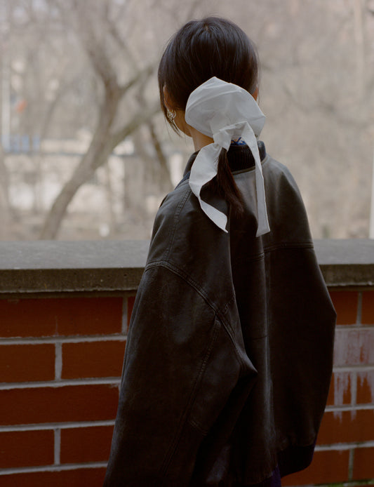 back of girl wearing white hair bow and black leather jacket